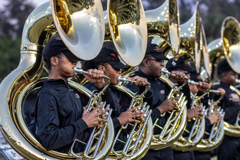 Marching sousaphone section playing in formation during an outdoor rehearsal