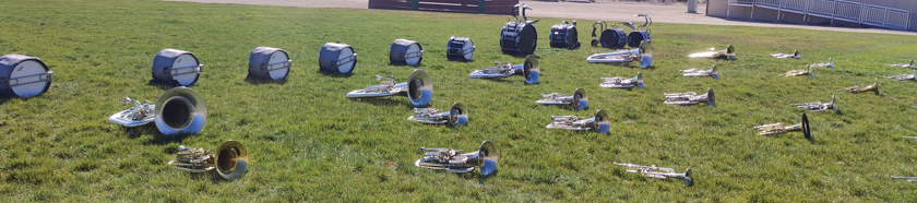 Marching band brass and percussion instruments resting on a grass practice field